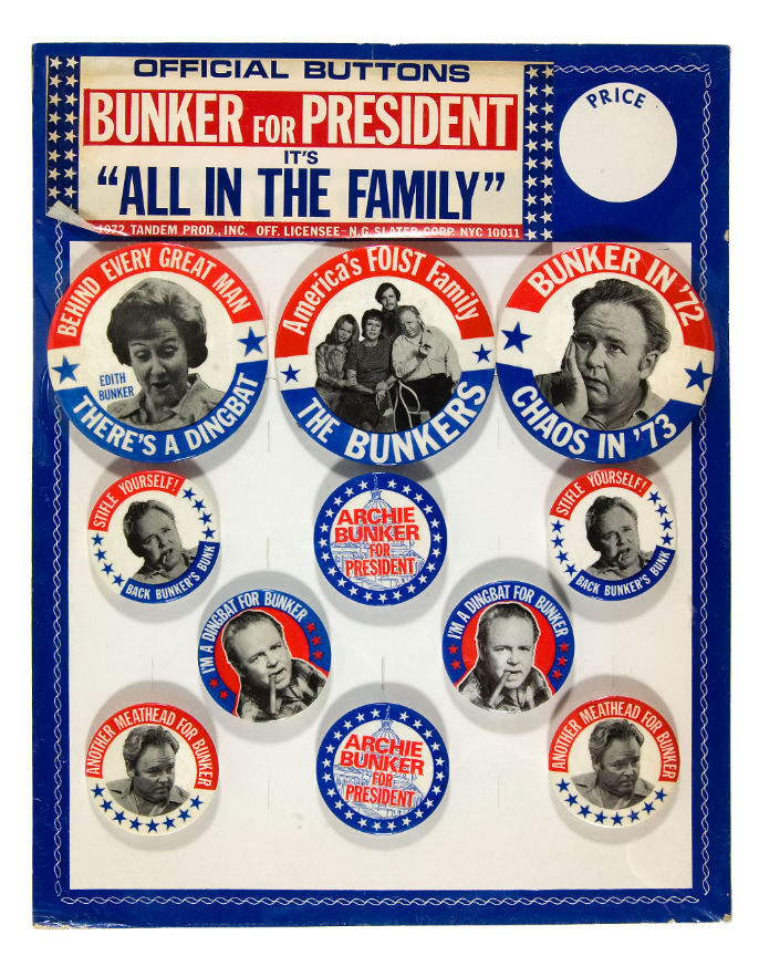 11×14″ stiff cardboard card with fold out easel reverse. “Official Buttons / Bunker for President / It’s ‘All In The Family’ / © 1972 Tandem Prod., Inc Off. Licensee – N.G. Slater Corp NYC 10011.” The card holds three 3.5″ buttons and eight 2⅛″ buttons. Most type is in all-caps . “Official Buttons” uses  Bold Extended. “Archie Bunker” is in .