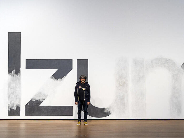 Taro Izumi posing in front of the mural that he and his team worked on in the Museum Tinguely in Basel.