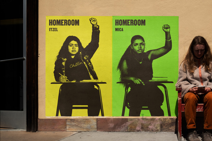 Wild posting of movie posters for Homeroom, designed by Mucho, with yellow and green backgrounds, featuring Mica Smith-Dahl and Itzel Mercado with raised fists.