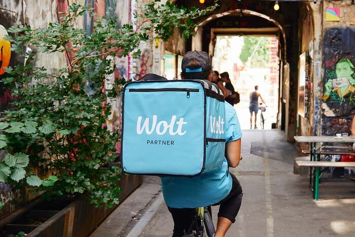 The Wolt logo paired with “Partner” in all-caps Omnes, on the bag of a courier.