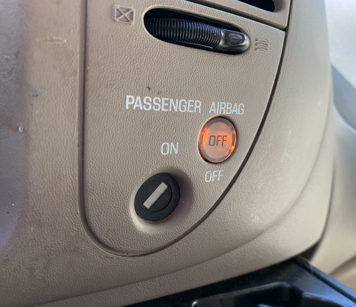 Passenger airbag deactivation switch, and indicator lamp, Ford F-150 pickup truck, 1997–2004. Pad printing over textured ABS plastic. The same part was used on the similar Ford Expedition, 1997–2003.
