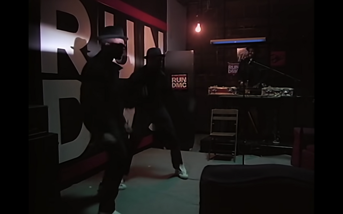 Still from the video for &ldquo;Walk This Way&rdquo;, with the logo painted on the wall. The letterforms in this version don&rsquo;t match the logo, or Franklin Gothic, for that matter.