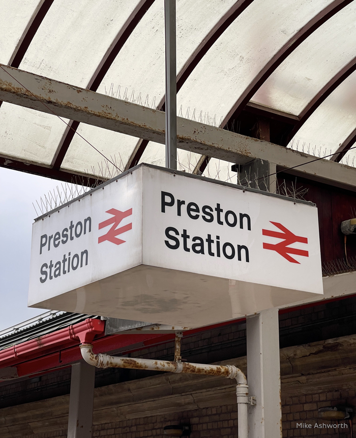 A four sides hanging internally illuminated box sign at Preston station featuring Rail Alphabet and the BR arrow logo, December 2021