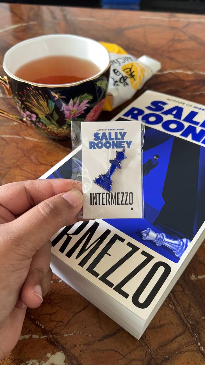 Promotional enamel pin and a paperback edition of the book