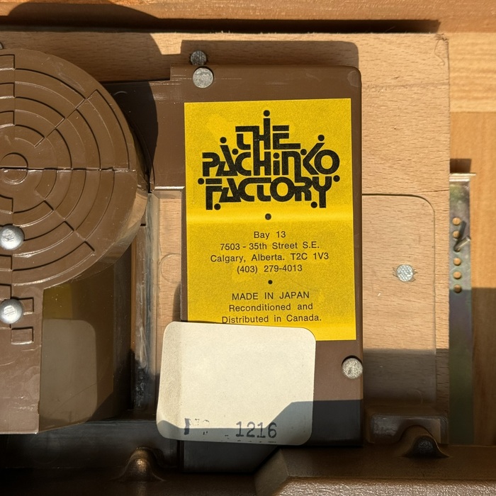 A sticker for The Pachinko Factory located amidst&nbsp;a&nbsp;pachinko machine mechanism.