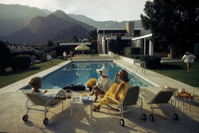 This photo is titled Poolside Gossip, with Nelda Linsk in yellow. It was taken by Slim Aarons, showing the modernistic Kaufmann Desert House designed by Richard Neutra.
