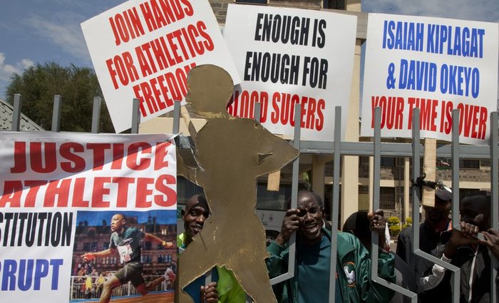 Athletes holds banners and look through the locked the gate at the Kenya Athletic offices in Nairobi, Kenya, Monday, Nov. 23, 2015. A group of Kenyan athletes occupied the headquarters of the national track and field federation on Monday, demanding the removal of its top officials in a protest against doping and corruption.