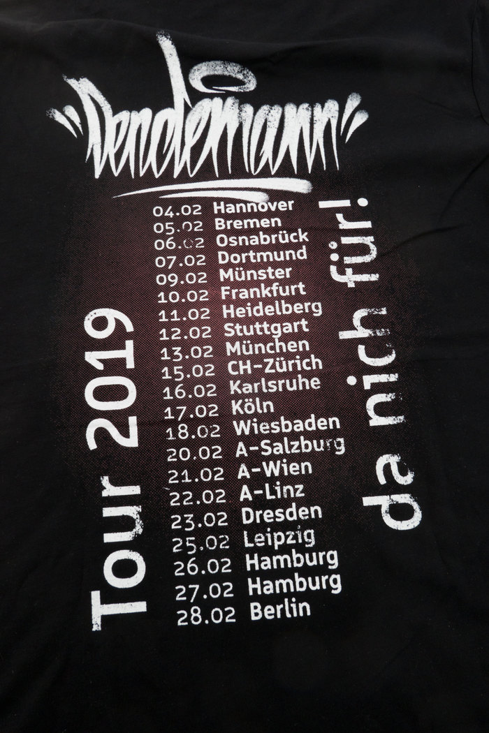 The tour shirt has been “vintaged” in a manual process, a technique first developed for the merchandise of Vom Vintage Verweht. The technique involves rubbing over a laser-print onto another surface with the help of solvent, such as aceton.