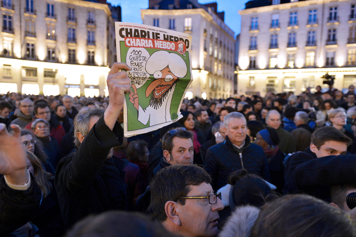 A man holds up an edition of Charlie Hebdo magazine as people gather on the Place Royale in Nantes, western France, on January 7, 2015, to show their solidarity with the victims of the attack on the offices of the satirical weekly in Paris. Muhammad’s speech bubble in the cartoon reads, in French, “A hundred lashes if you don’t die laughing.”