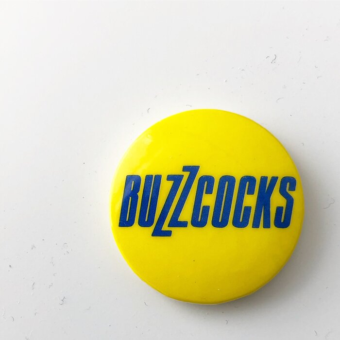 Pinback button posted by Malcolm Garrett to commemorate Buzzcocks singer Pete Shelley, 1955–2018.