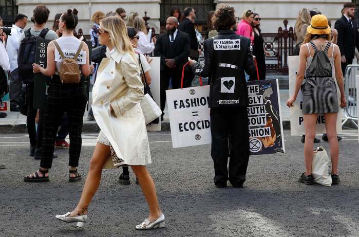 September 2019. A show-goer walks past Extinction Rebellion protesters as they demonstrate against London Fashion Week.